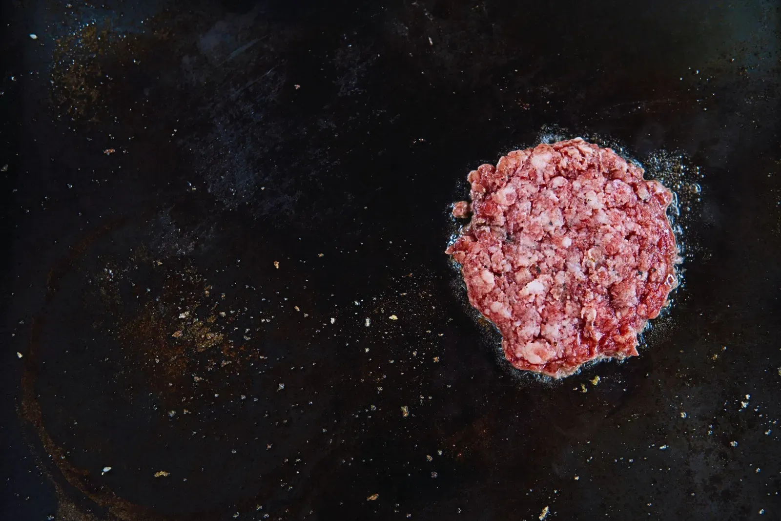 Patty brisket mentah di atas griddle panas